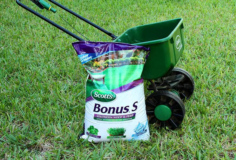 a bag of lawn fertilizer leaning against a dispenser in the middle of a lawn