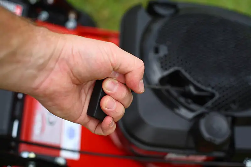 a person pulling the starter cord to start a lawnmower