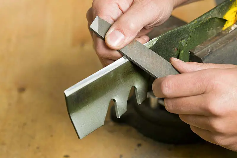 a person manually sharpening a blade using a file and a vice