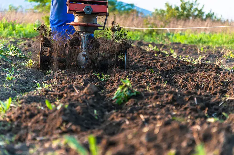 a rototiller moving along the grass in order to flip the soil