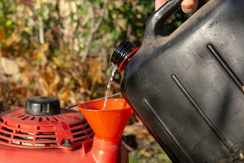person pouring oil into a lawnmower