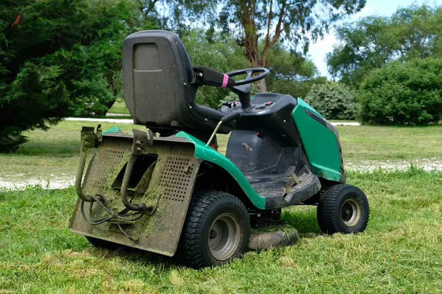 a riding mower resting in on some uncut grass